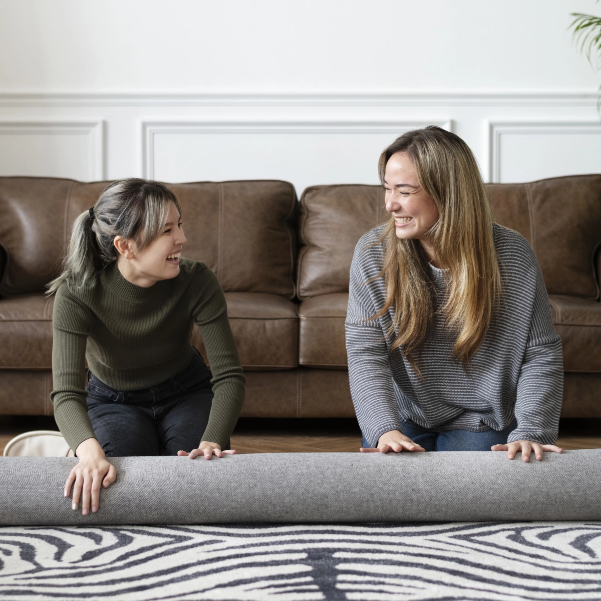 Deux femmes travaillent ensemble pour aplatir un tapis sur un parquet dans un salon confortable.