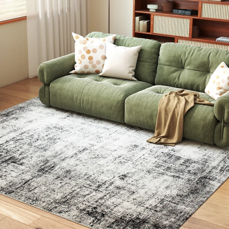 Canapé en velours vert sur un tapis texturé gris-noir avec une bibliothèque et une lumière naturelle en arrière-plan.