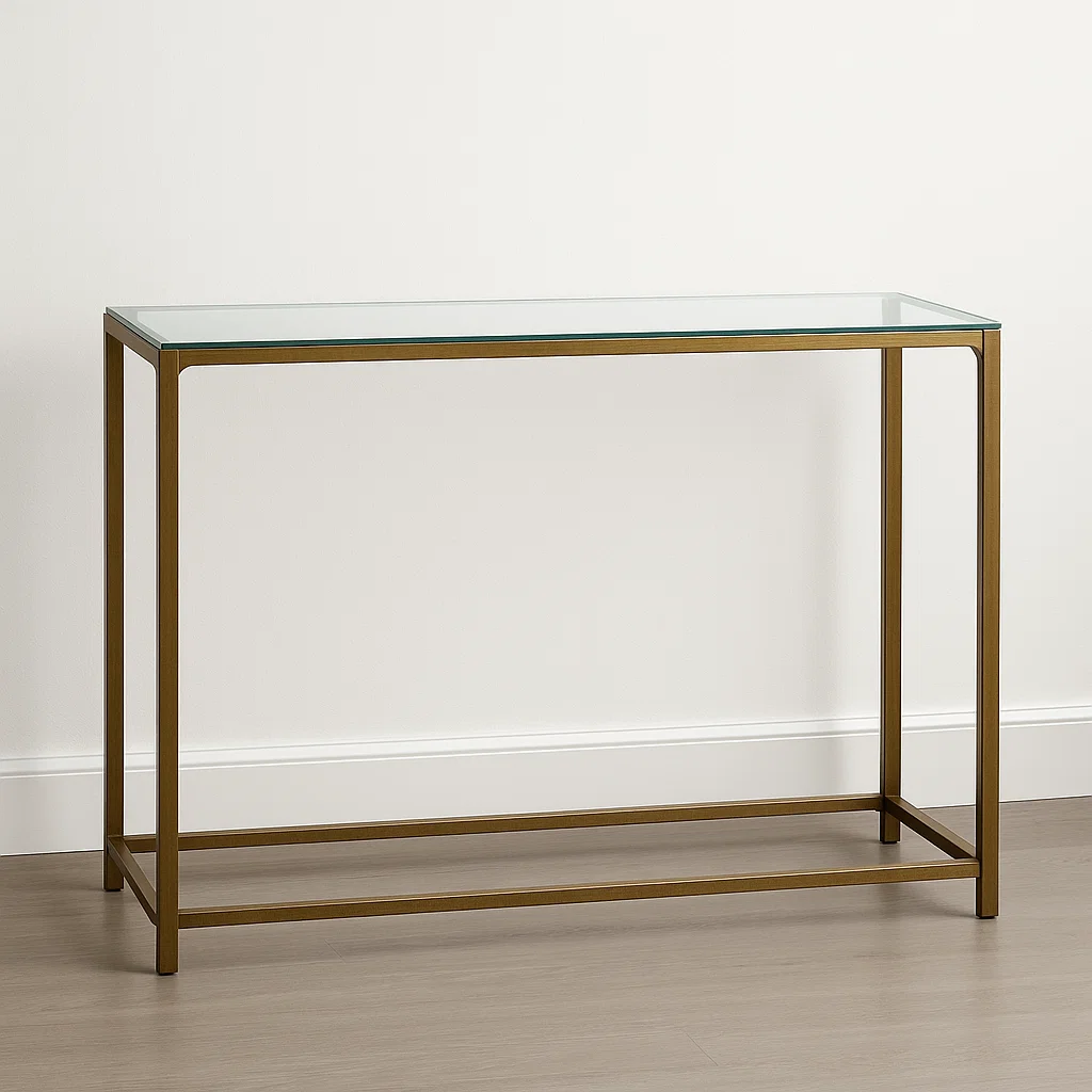 Table console minimaliste avec plateau en verre et fine structure en métal bronze contre un mur clair et un sol en bois.