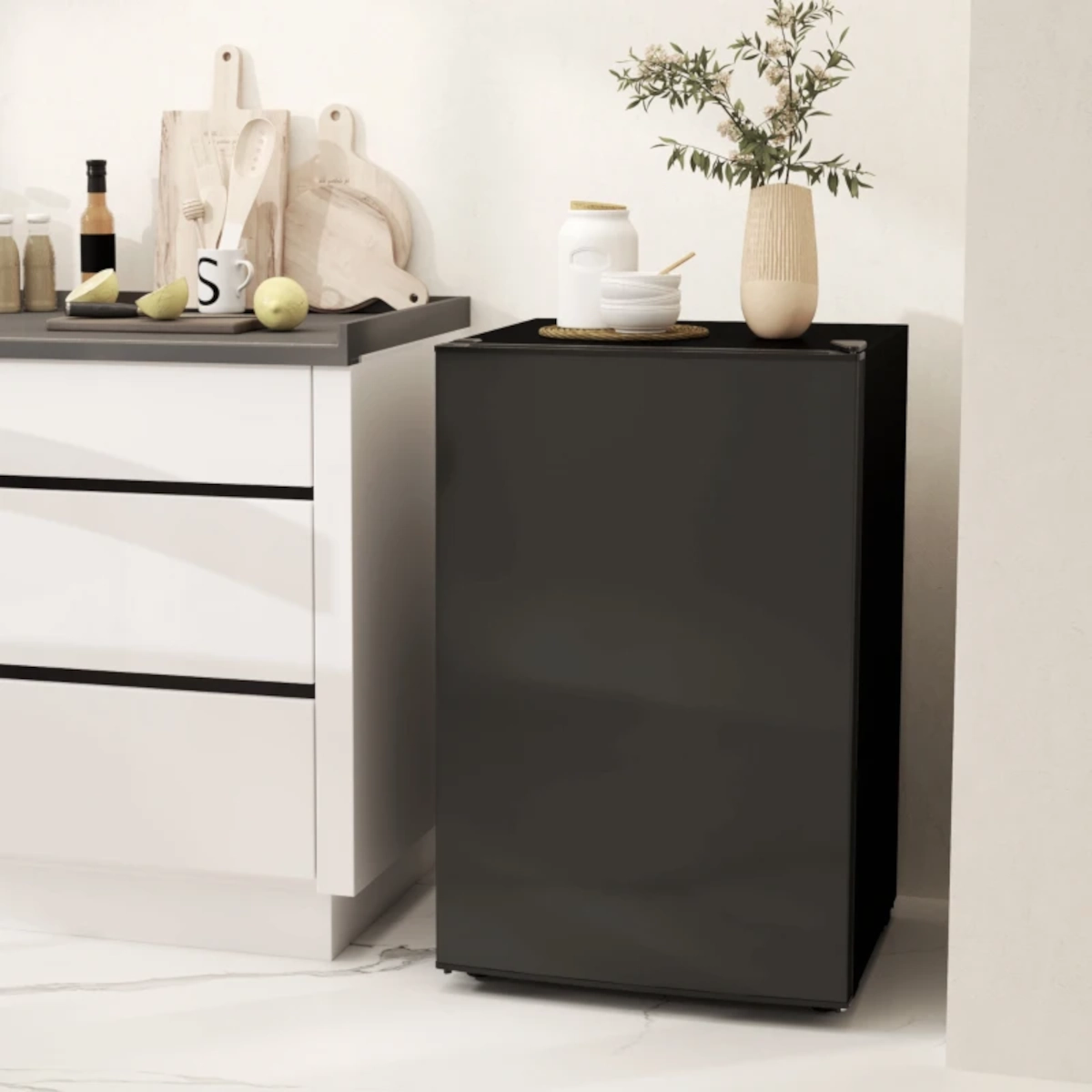 Mini-frigo noir mat placé à côté du comptoir de cuisine avec des objets de décoration sur le dessus.