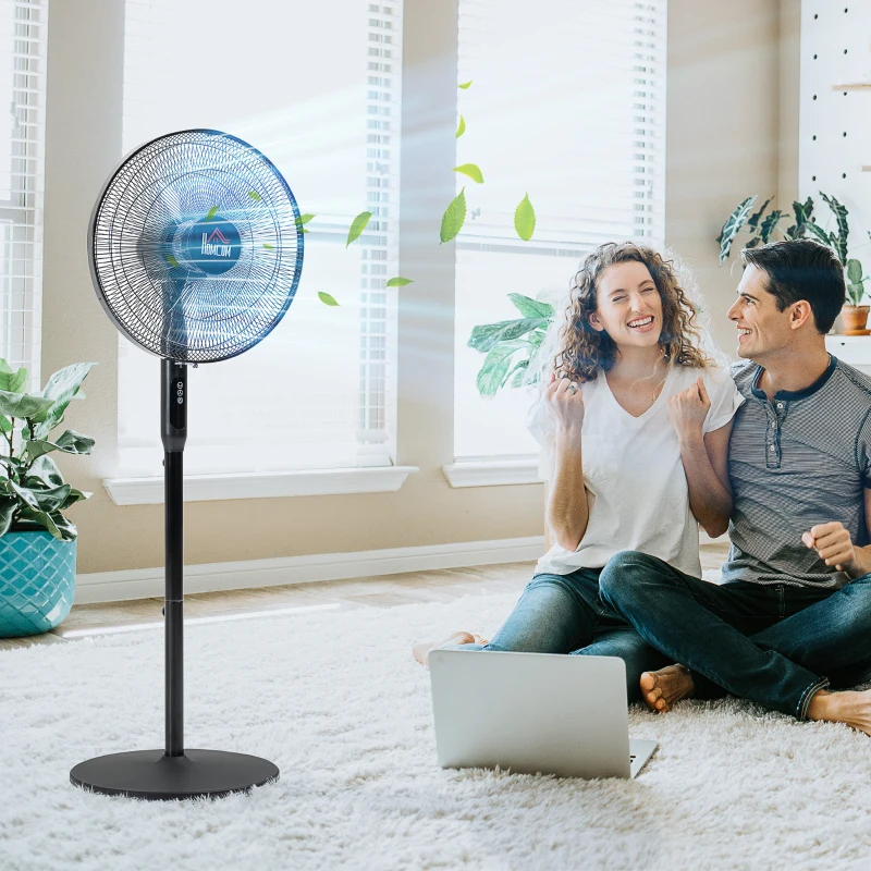 Un couple profite de la brise fraîche d'un ventilateur électrique sur pied à l'intérieur.