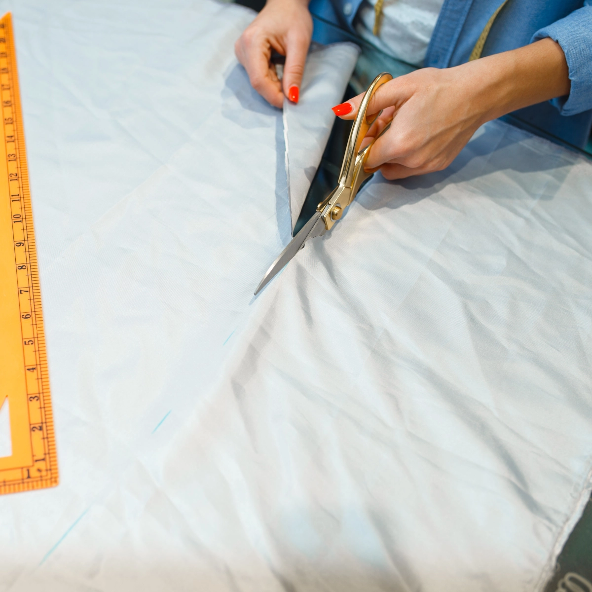 Gros plan de ciseaux coupant du tissu bleu clair le long d'une ligne de mesure à la craie.