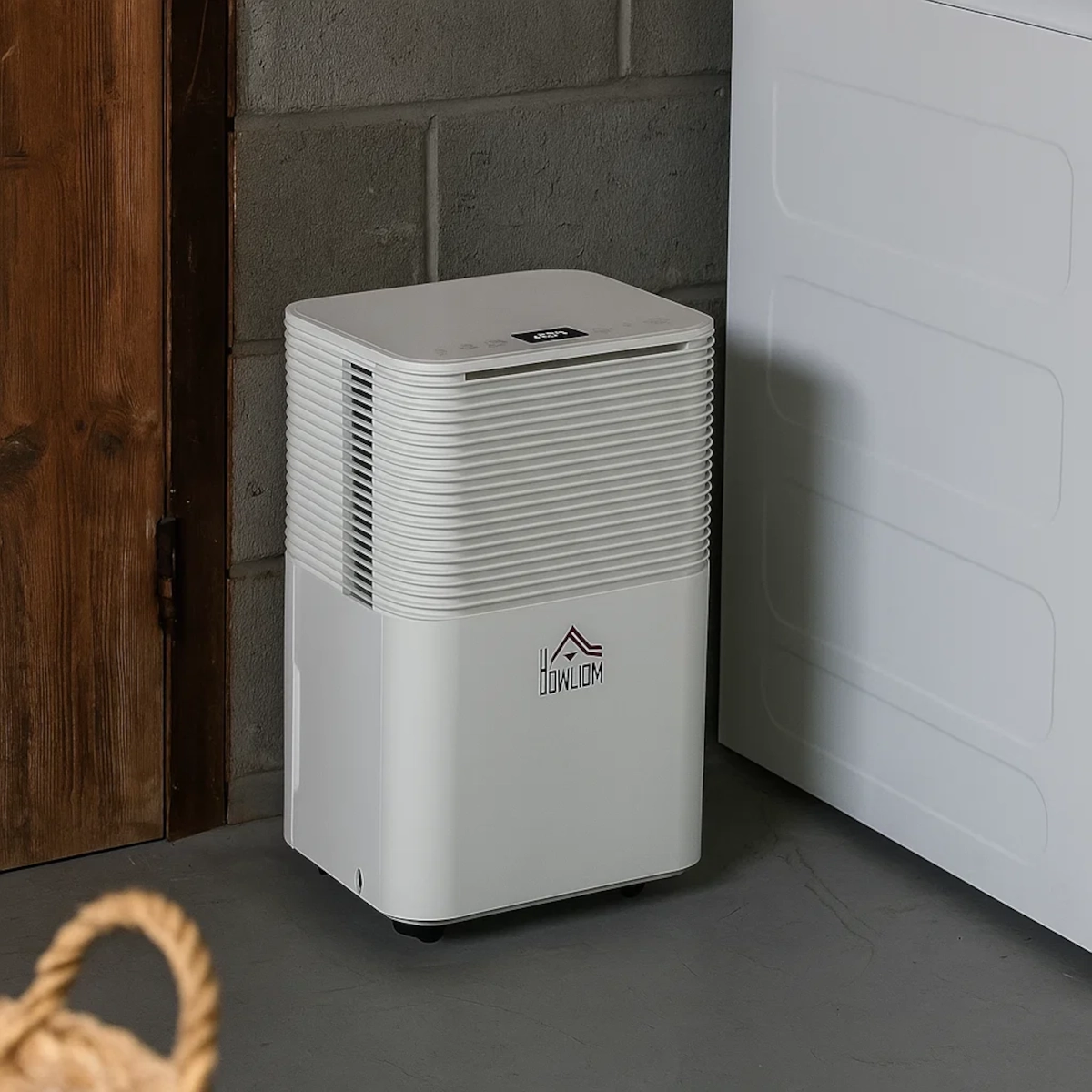 Déshumidificateur HOMCOM blanc placé à côté d'un lave-linge dans une buanderie au sous-sol.