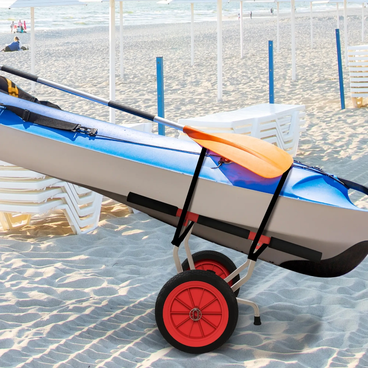 Kayak bleu fixé sur un chariot à roues rouges posé sur une plage de sable près de transats blancs.