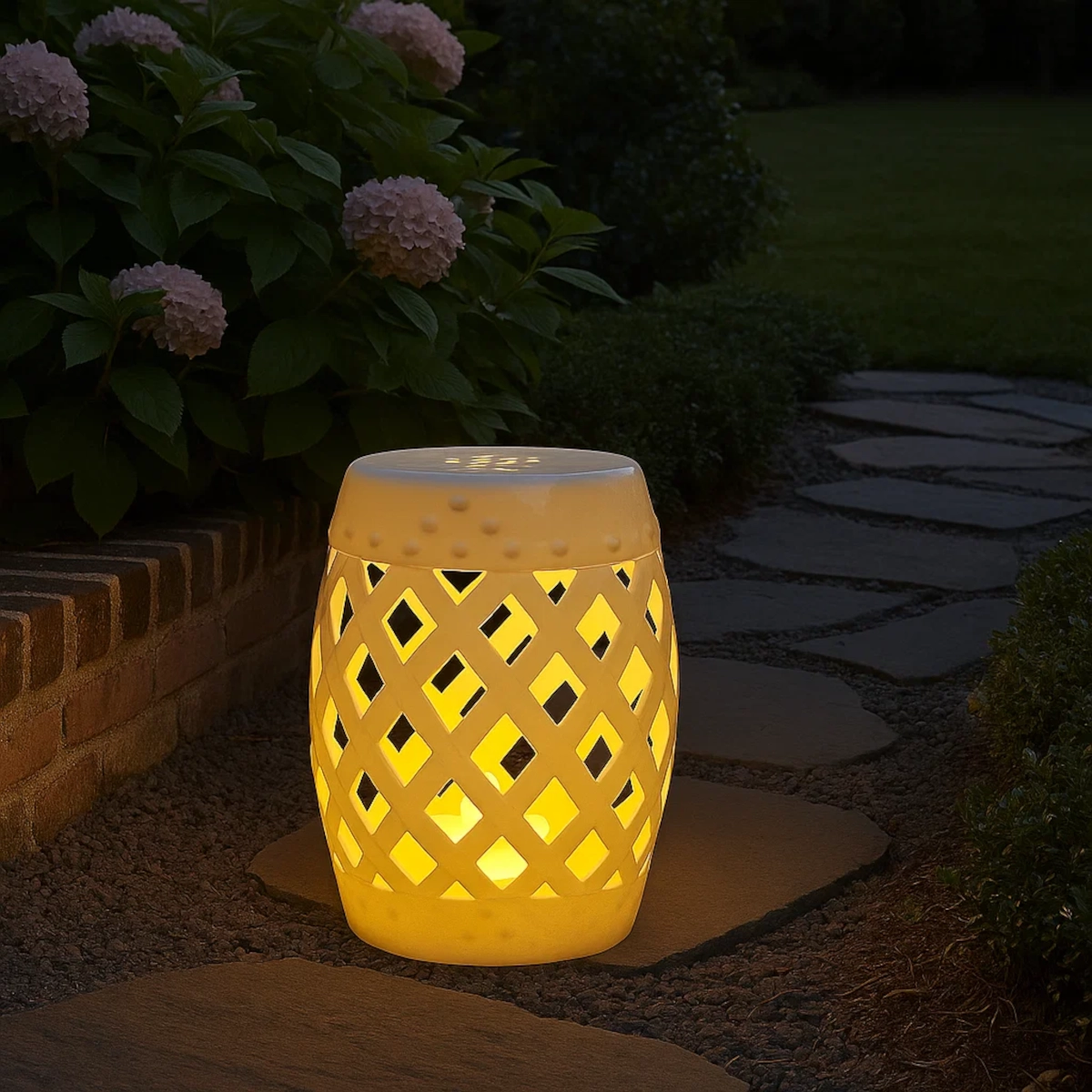 Tabouret de jardin blanc illuminé le long d'un sentier de jardin, entouré de buissons de hortensias en fleur.