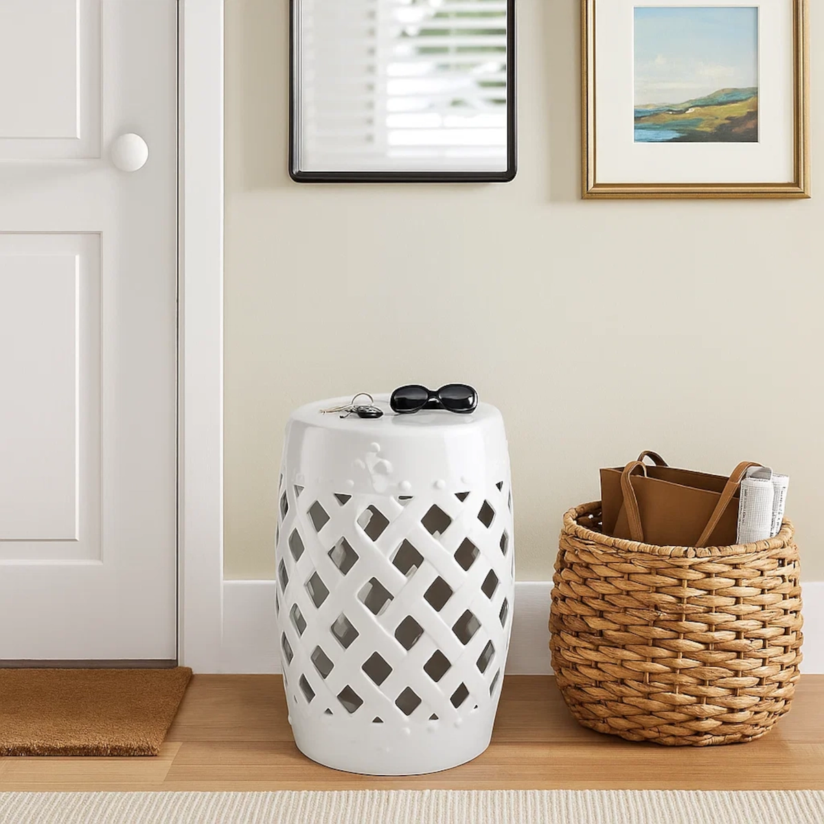Entrée avec un tabouret de jardin blanc brillant, un panier de transport, des lunettes de soleil et une œuvre d'art encadrée sur le mur.