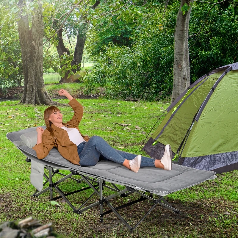 Lit de camping pliant avec matelas épais et oreiller attaché installé en extérieur sur de l'herbe.