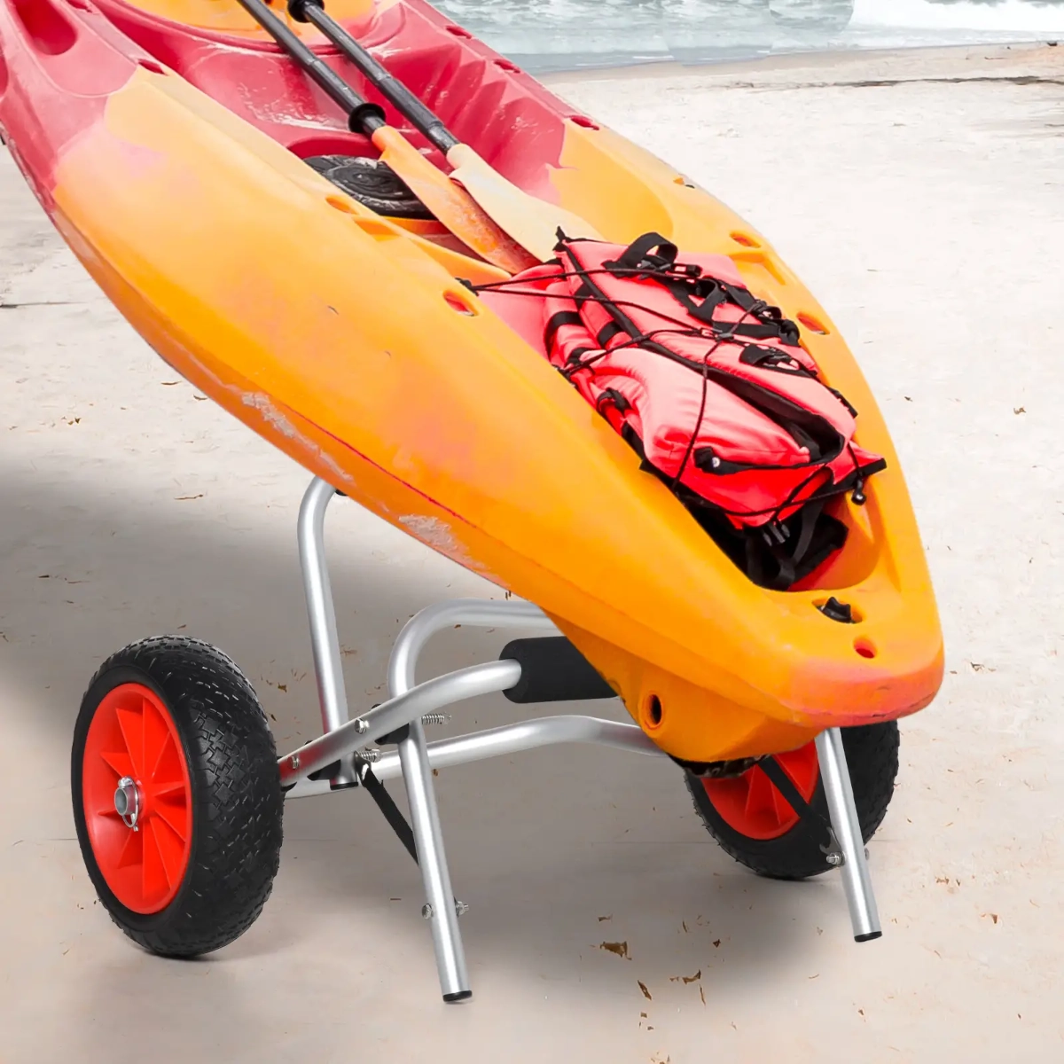 Kayak orange reposant sur un chariot pliant compact à roues rouges avec un arrière-plan de plage.