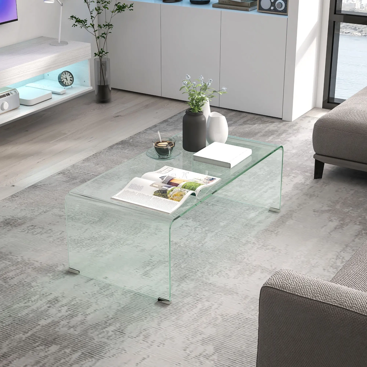 Table basse en verre transparent avec des bords arrondis placée dans un salon moderne minimaliste.