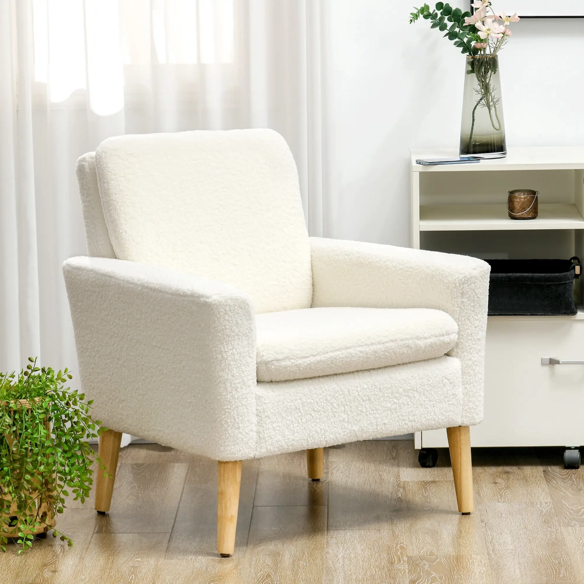 Fauteuil d'appoint en bouclé crème avec des pieds en bois clair dans un coin doucement éclairé avec des plantes d'intérieur.