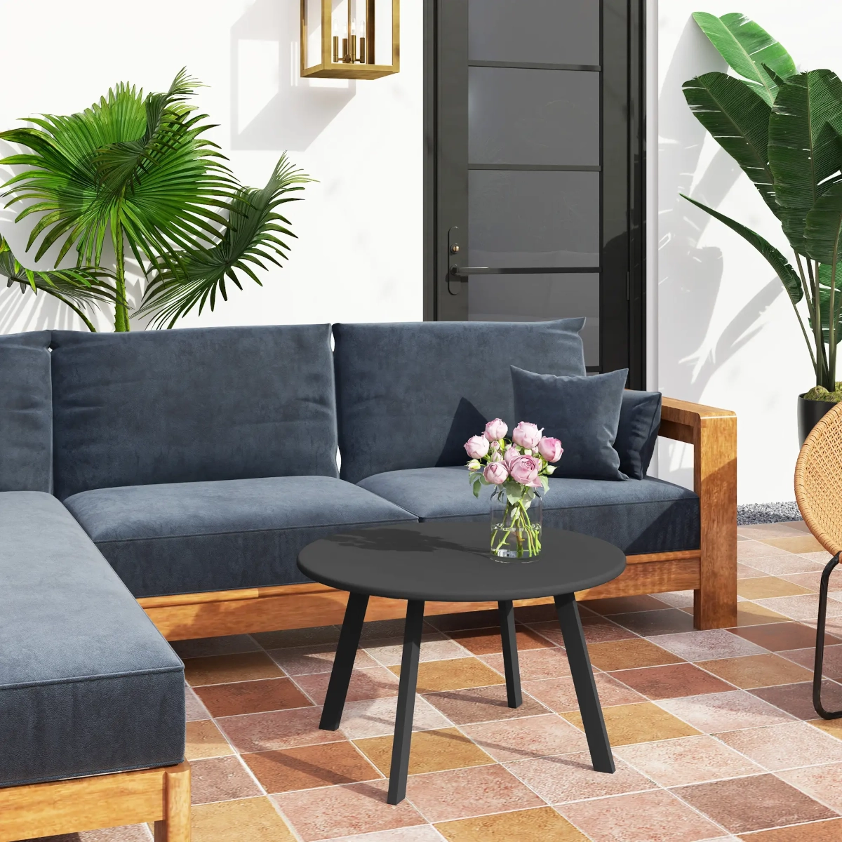 Table basse noire ronde avec un vase de roses roses dans un coin de patio aménagé avec des coussins bleus.