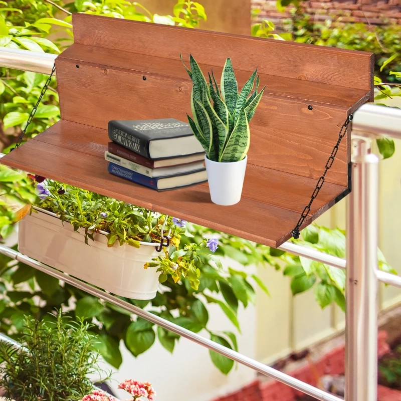 Table pliante en bois sur le garde-corps du balcon avec des livres et une plante en pot, entourée de feuillage vert.