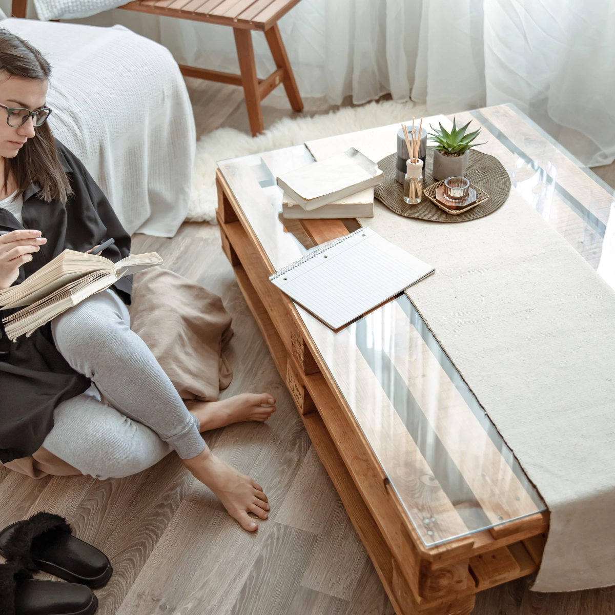Personne lisant un livre à côté d'une table basse avec des cahiers, une plante et des accessoires de décoration.