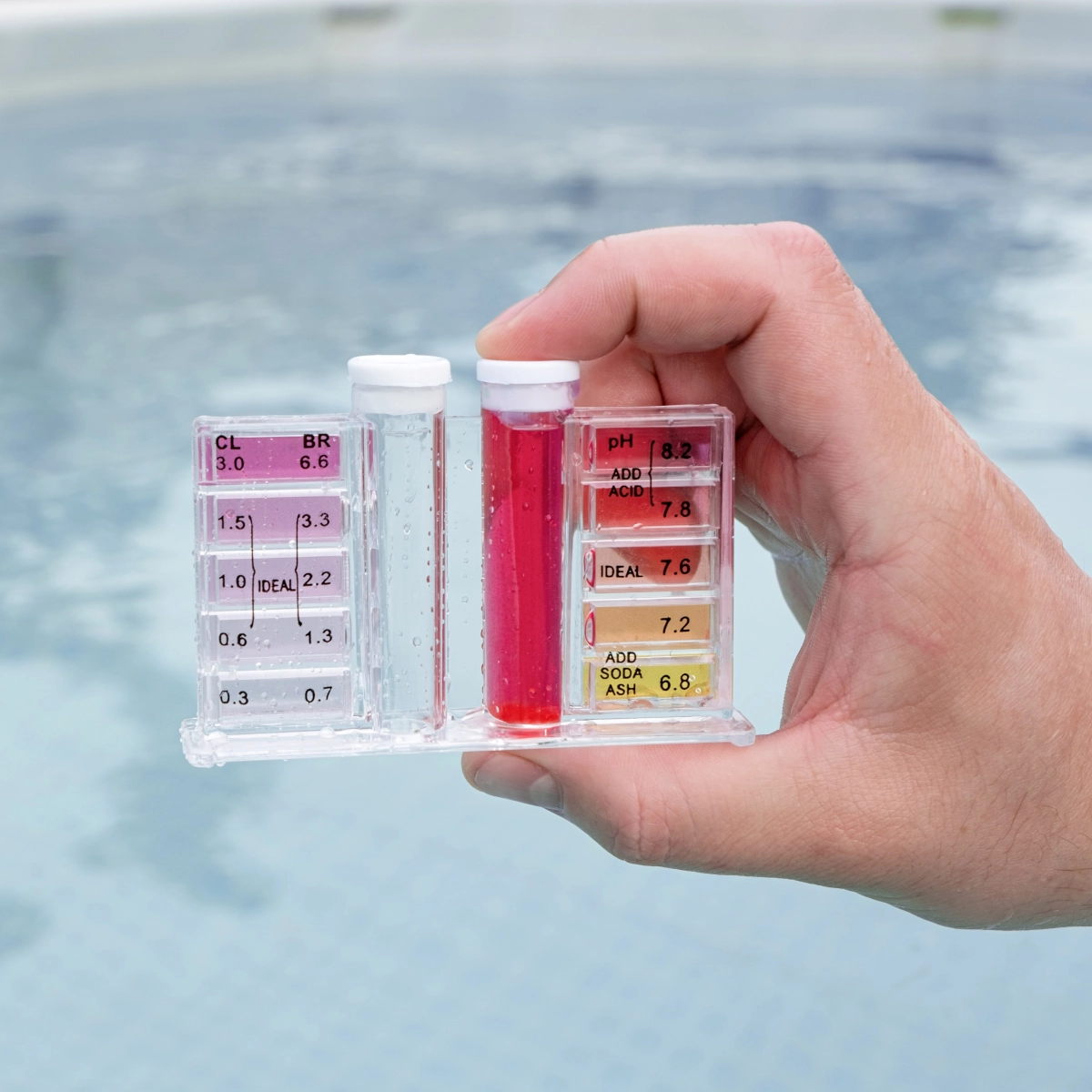 Une main tient un kit de test de l'eau de piscine près d'un bain de plongée froide pour surveiller la qualité de l'eau.