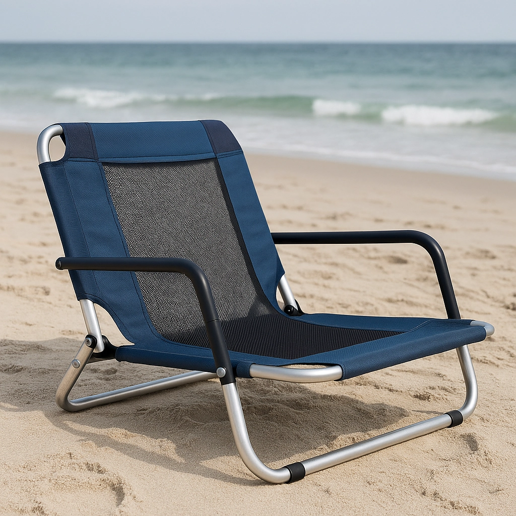 Chaise de plage basse avec dossier en mesh sur le sable, face aux vagues de l’océan sous un ciel nuageux.