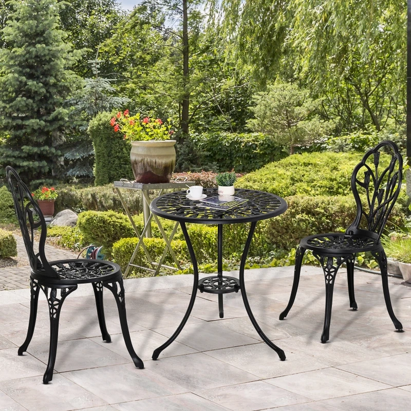 Table et chaises de terrasse en aluminium moulé noir sur une terrasse en pierre dans un jardin verdoyant.