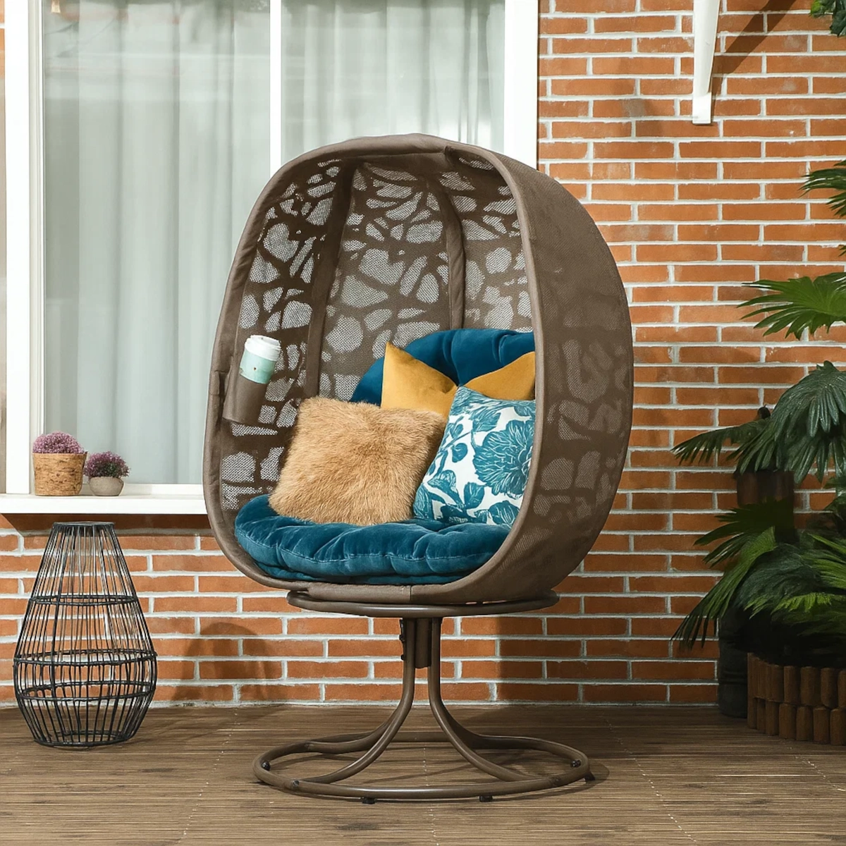 Fauteuil œuf stylé avec coussins turquoise et moutarde, oreillers floraux, sur une terrasse en bois.