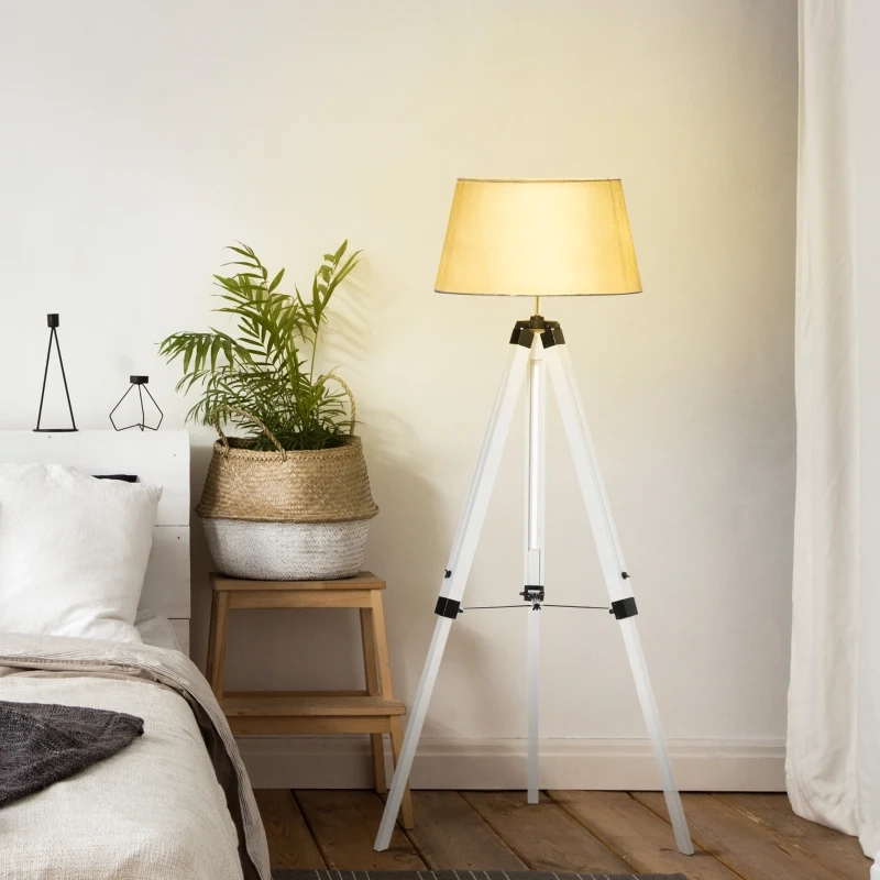 Chambre douillette avec lampadaire blanc tripode et abat-jour en tissu à côté du lit et d’une plante en pot.