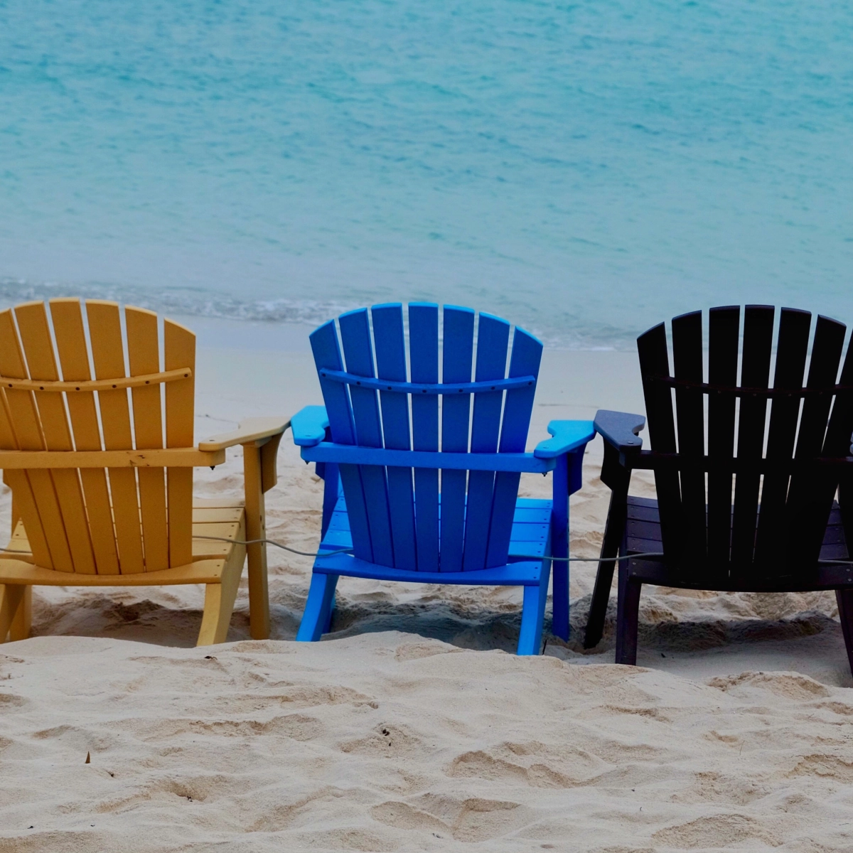 Diverses chaises de plage aux designs variés disposées sur une plage sablonneuse.