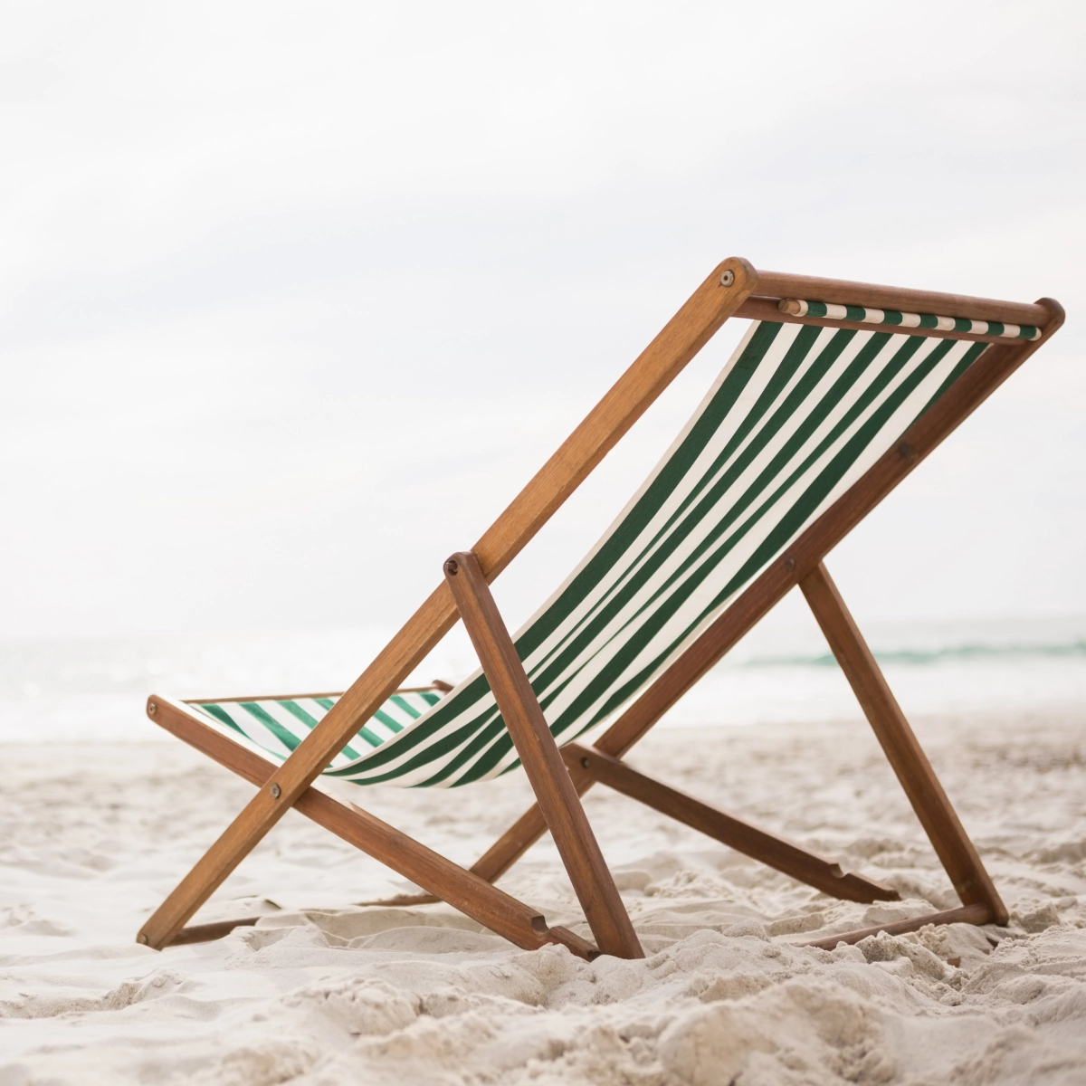 Chaise de plage classique en bois basse avec un tissu à rayures vertes sur une plage de sable blanc.